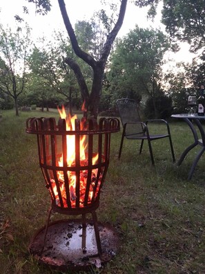 A metal fire pit with flames, surrounded by grass and trees. - Vacation apartment Linde (2 persons) - Ferienwohnungen May (Plankenfels)