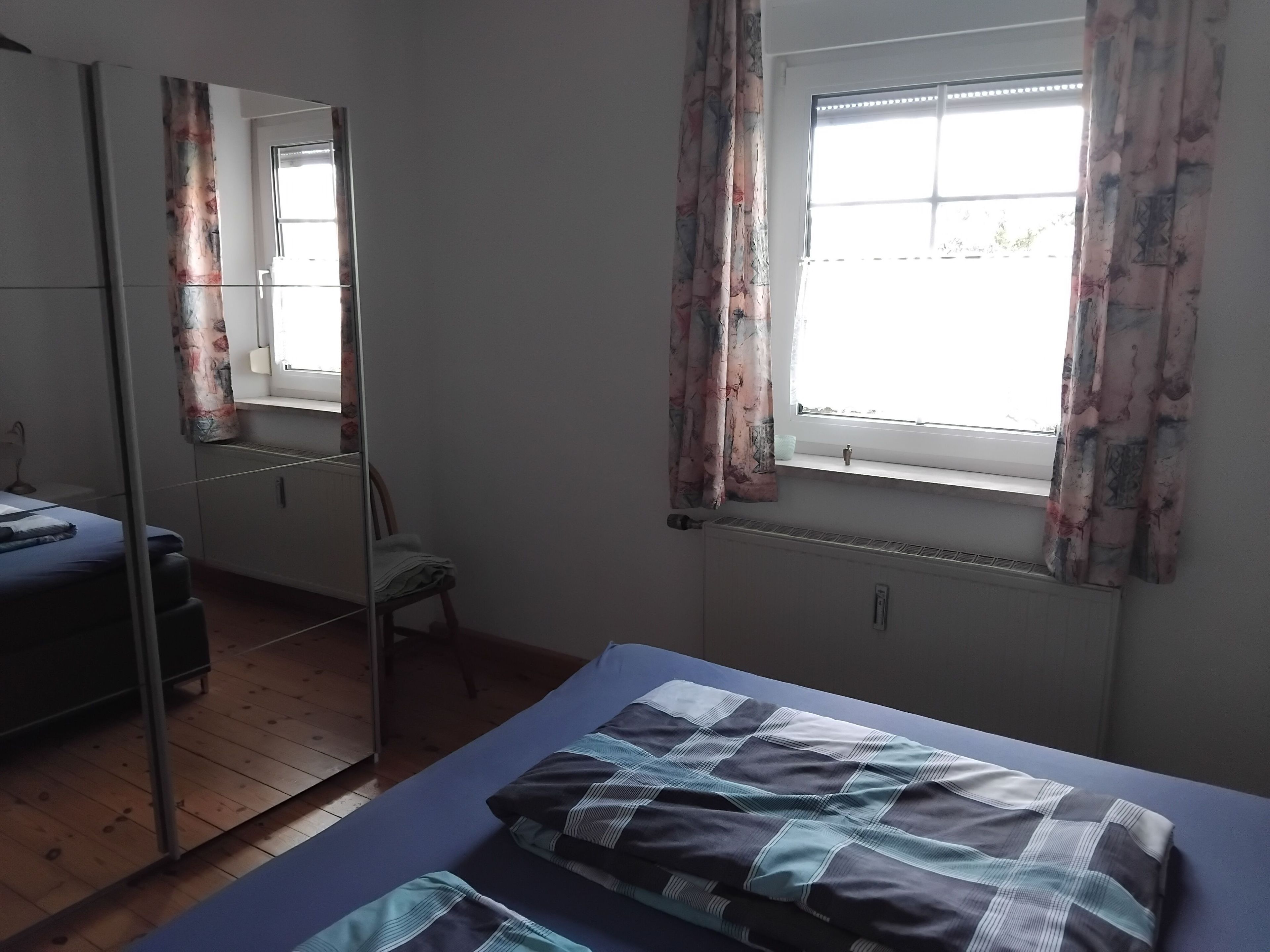 A bedroom with a bed, a chair, a window with curtains, and a radiator.