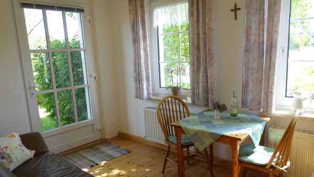 Um quarto acolhedor com piso de madeira, um sofá marrom, uma mesa de jantar com cadeiras e uma janela com cortinas.