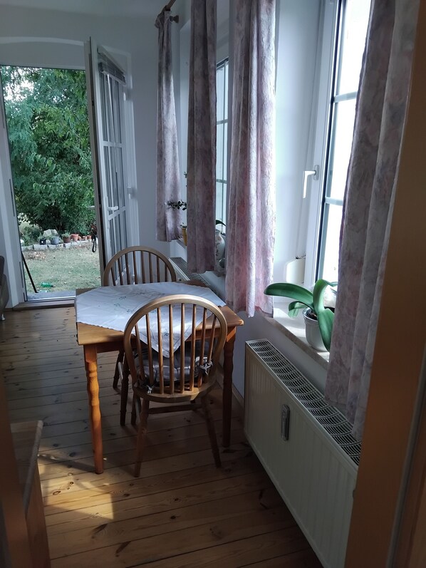 Una habitación con una mesa y sillas de madera, un radiador y una ventana con cortinas.