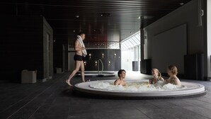 Un espace piscine intérieure moderne, où l’on voit une personne qui marche et d’autres personnes se détendre dans l’eau.