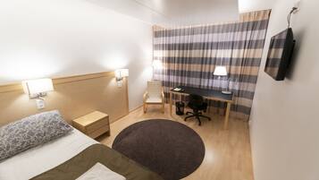 Una habitación de hotel con cama, escritorio, silla, televisor y ventana con cortinas a rayas.