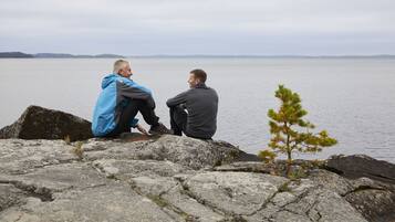Two people sitting on rocks by a lake with a small tree nearby.