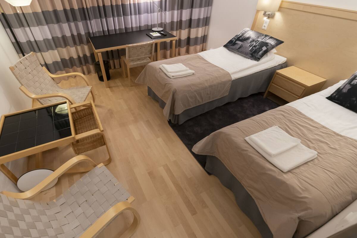 Een hotelkamer met twee bedden, een bureau, een stoel en een klein tafeltje.