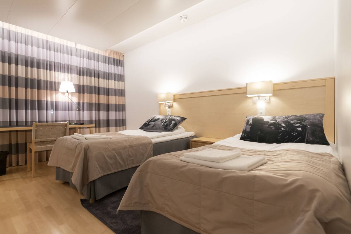 Een hotelkamer met twee bedden, een bureau, een stoel en een gestreept gordijn.
