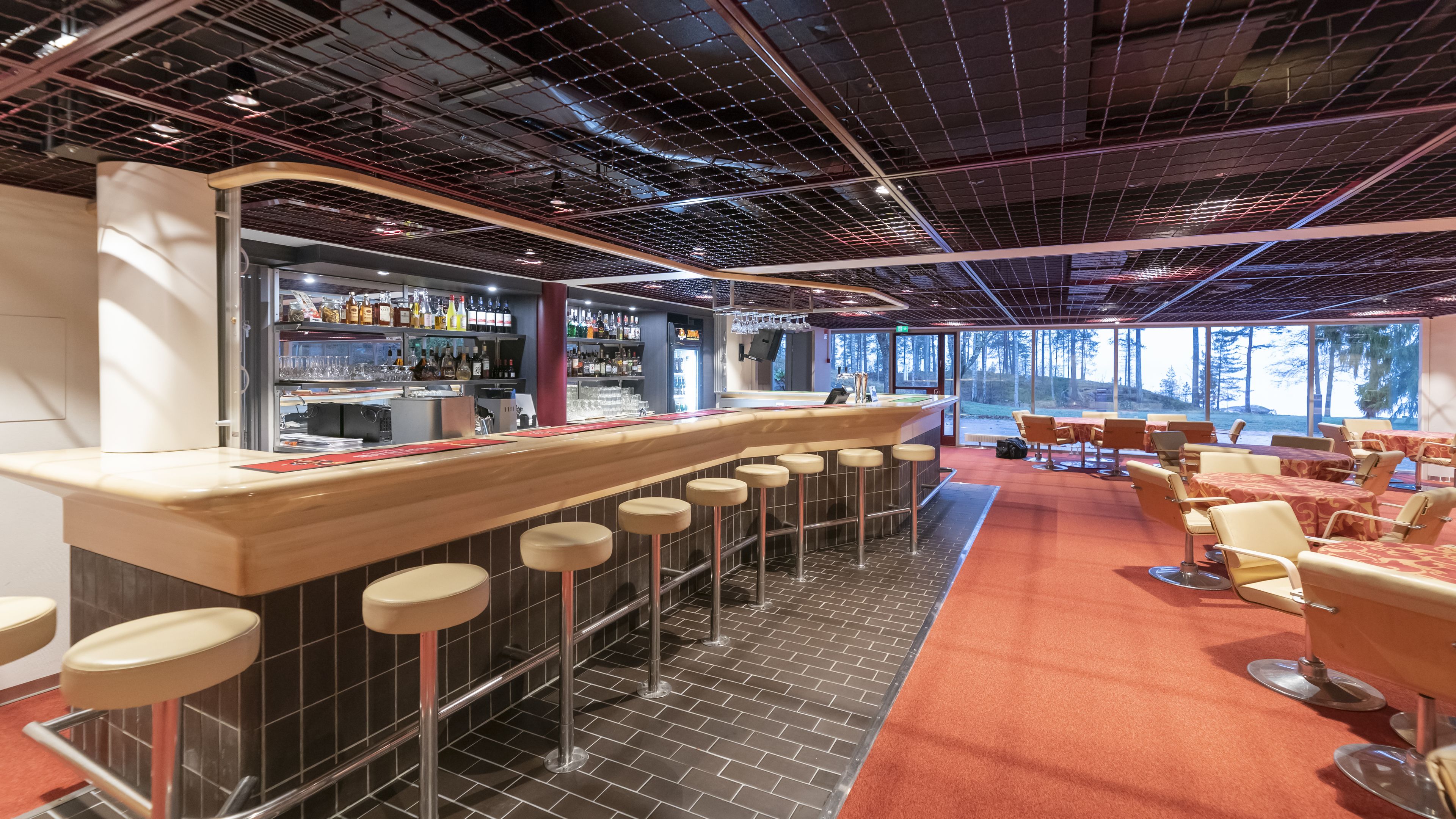 A modern bar area with a counter, stools, and a seating area with tables and chairs.