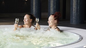 Deux personnes dans un jacuzzi, entourées de bulles, tenant chacune un verre contenant un liquide transparent.