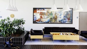 Un hall d’entrée moderne avec un canapé en cuir noir, une table basse en bois, des lampes suspendues et un grand tableau abstrait accroché au mur.