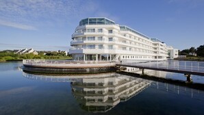 A multi-story waterfront hotel with balconies, a covered deck, and a reflection in the water. - Nice T2 view on the port of Crouesty (Arzon)