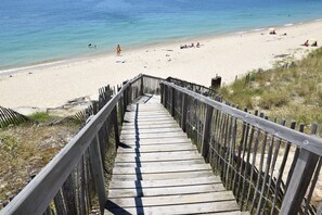 Eine Holztreppe führt zu einem Strand mit klarem, blauem Wasser.