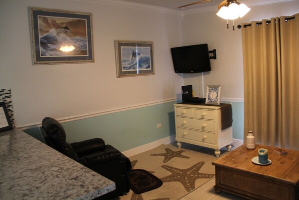 A living room with a television mounted on the wall, a starfish-patterned rug, a wooden coffee table, and a white dresser. - Fish Heaven- 2 bed, 2 bath in KCB with boat lift, ice machine & cabana club (Key Colony Beach)