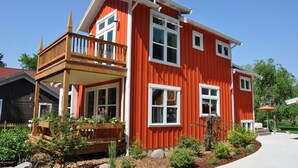 Une maison à deux étages, avec une façade rouge, un balcon en bois et un jardin bien entretenu.