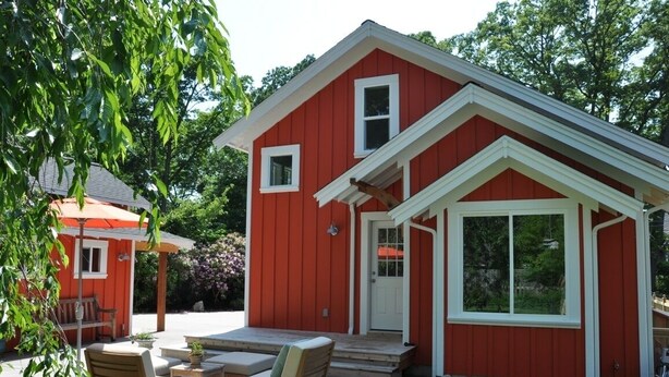 Une maison rouge avec un porche, un petit patio avec des chaises et un jardin.