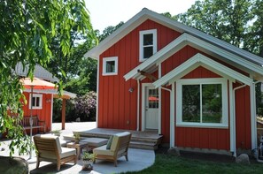 A red house with a porch, a small patio with chairs, and a garden.