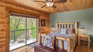 Un dormitorio de cabaña de madera con una cama, un banco, un ventilador de techo y vistas al exterior.