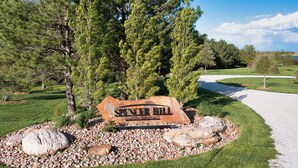 Señal para el Spencer Hill Golf Club, rodeado de césped cuidado, árboles y un camino de grava.