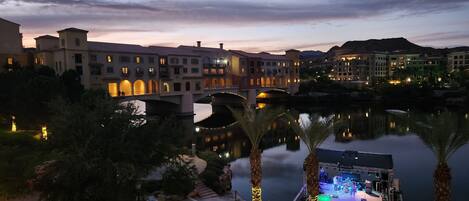 A riverside hotel with a stage for events, palm trees, and a bridge.