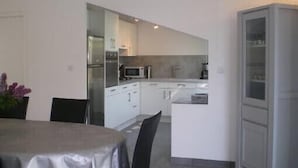 A modern kitchen with white cabinets, a microwave, and a built-in oven. There is a dining area with a table and chairs.