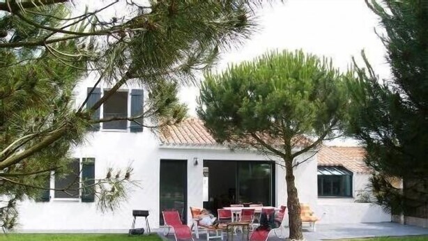 A white house with a tiled roof, a patio with red chairs, and a lawn.