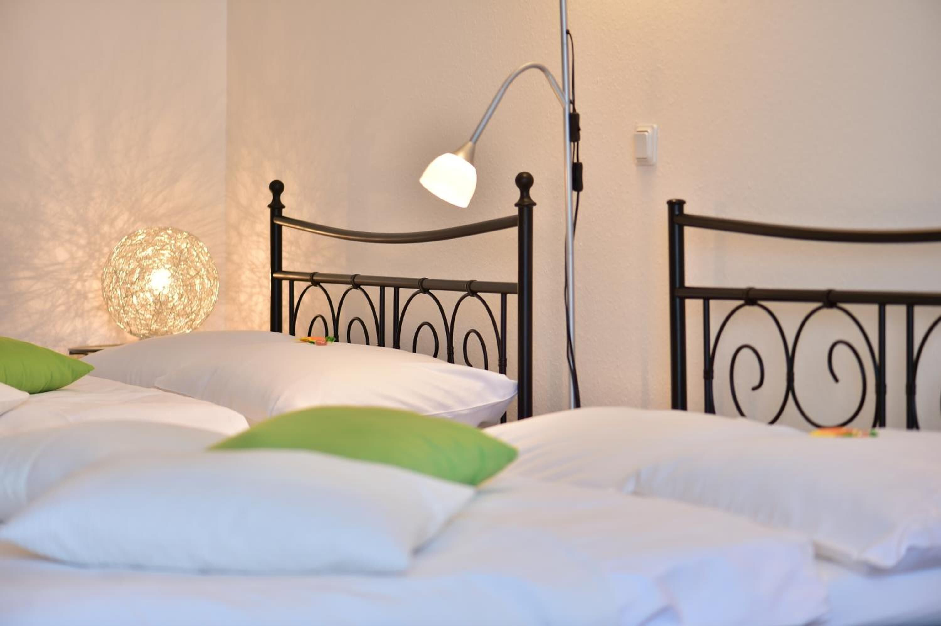 Una cama bien tendida con almohadas blancas y verdes, un cabecero de metal negro y una lámpara de noche.