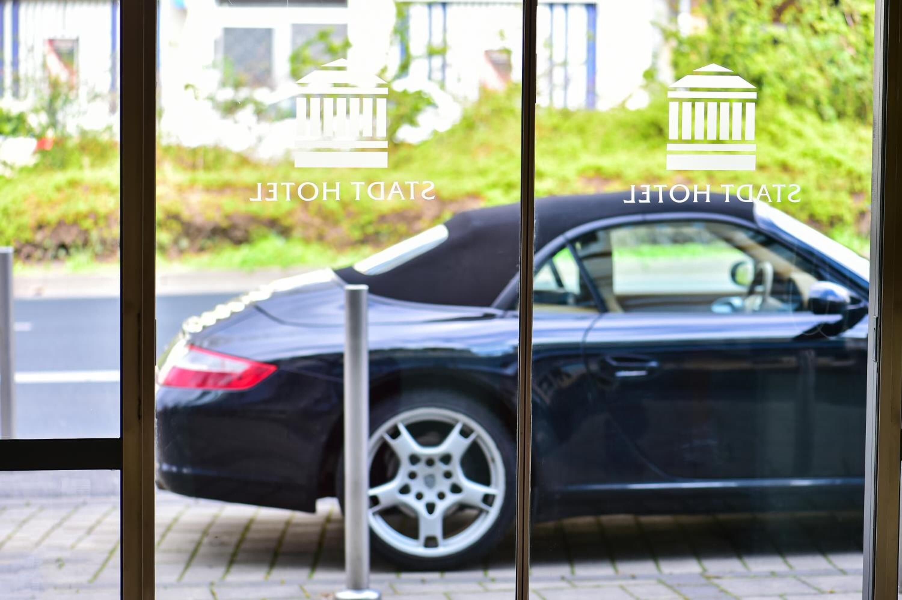 A black car parked outside a building with a glass door.