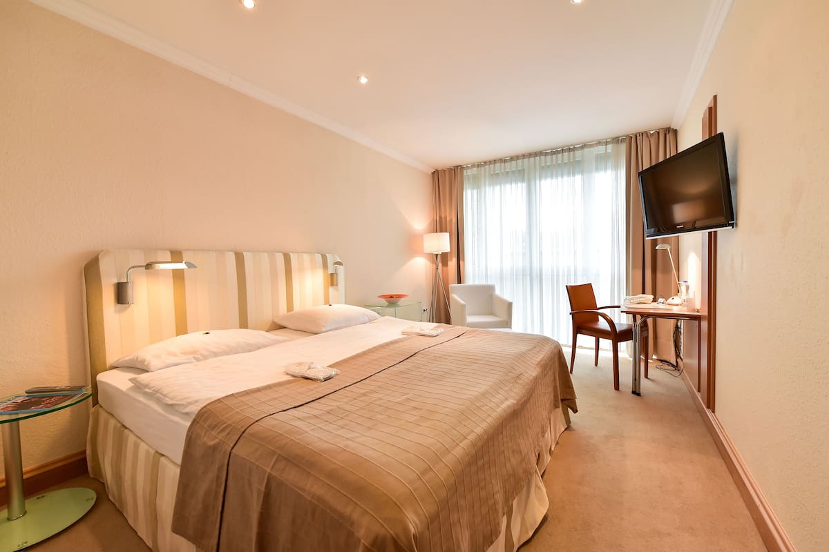 A hotel room with a bed, a desk, a chair, a TV, and a lamp.