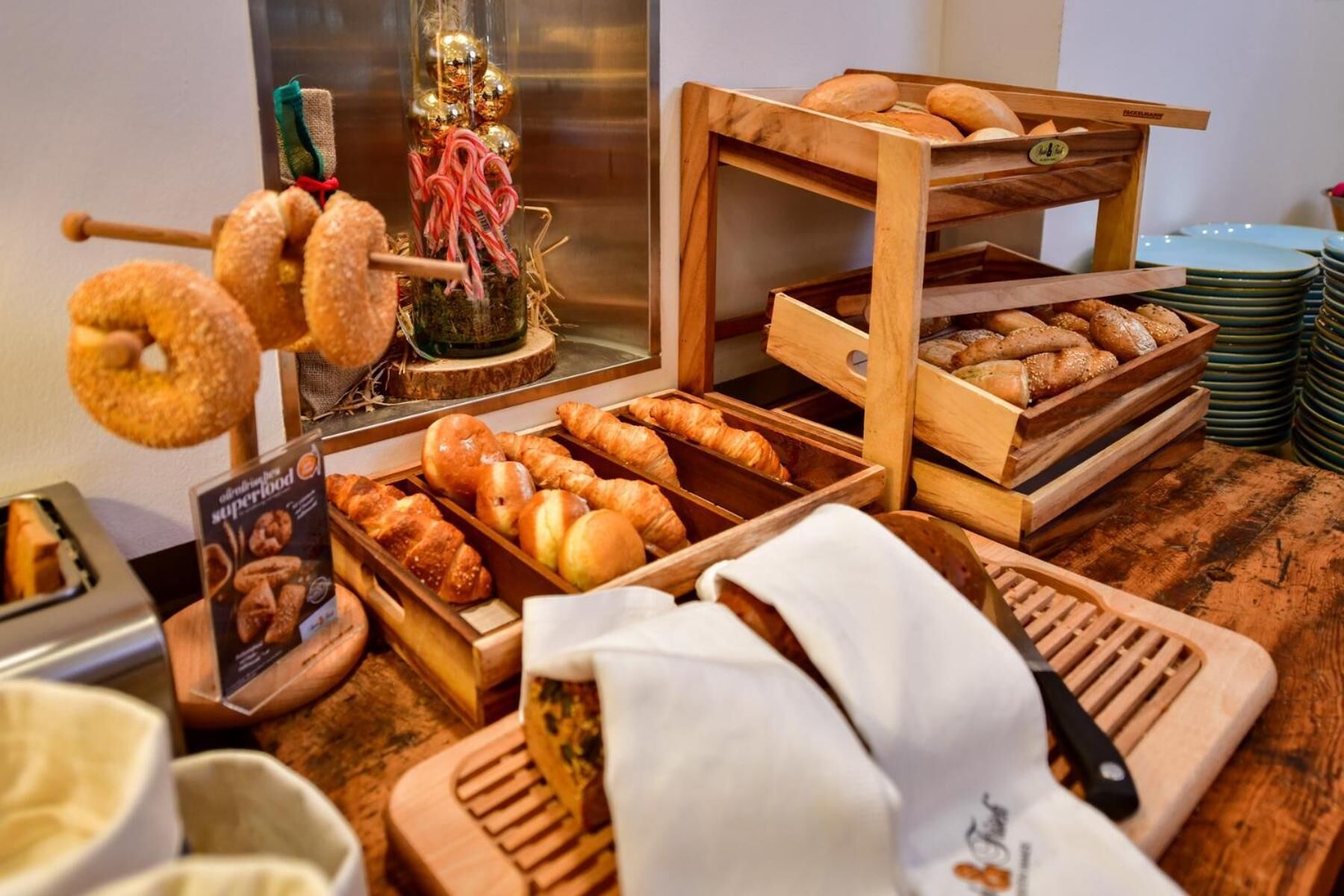 Vitrine de padaria com diversos produtos de panificação, incluindo croissants e donuts, dispostos em suportes e bandejas de madeira.