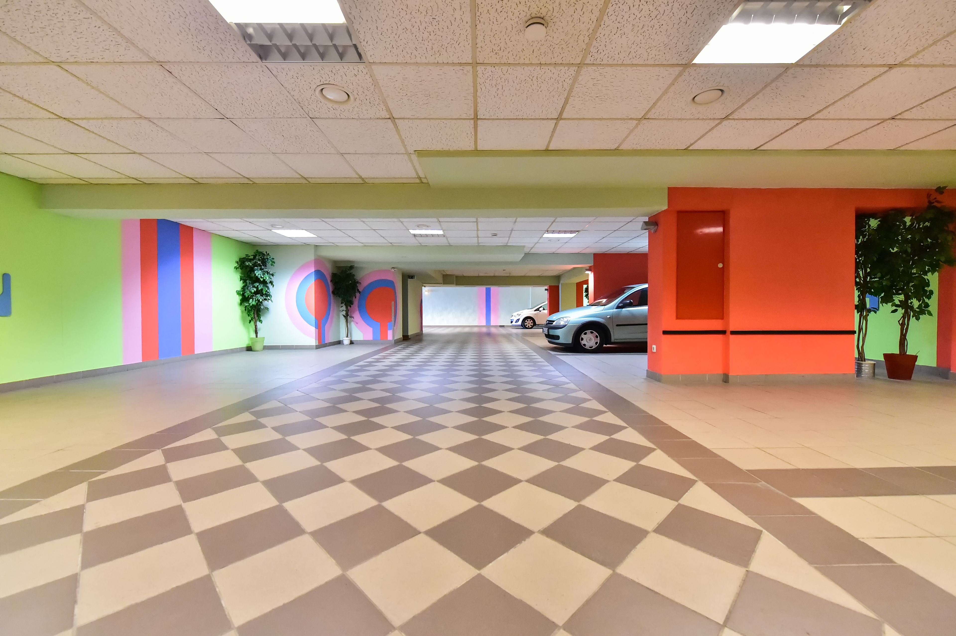 A spacious indoor area with a checkered floor, colorful walls, and potted plants.
