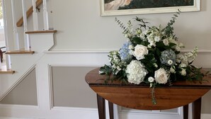 A staircase with white railings and a wooden handrail, leading to a landing with a wooden table displaying a floral arrangement.