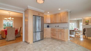 A modern kitchen with wooden cabinets, a stainless steel refrigerator, and a dining area with a table and chairs.