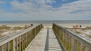 A wooden boardwalk leading to a beach with people relaxing on the sand and chairs.