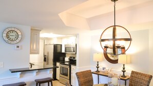 A modern kitchen with white cabinetry, stainless steel appliances, and a dining area with wicker chairs and a glass table.