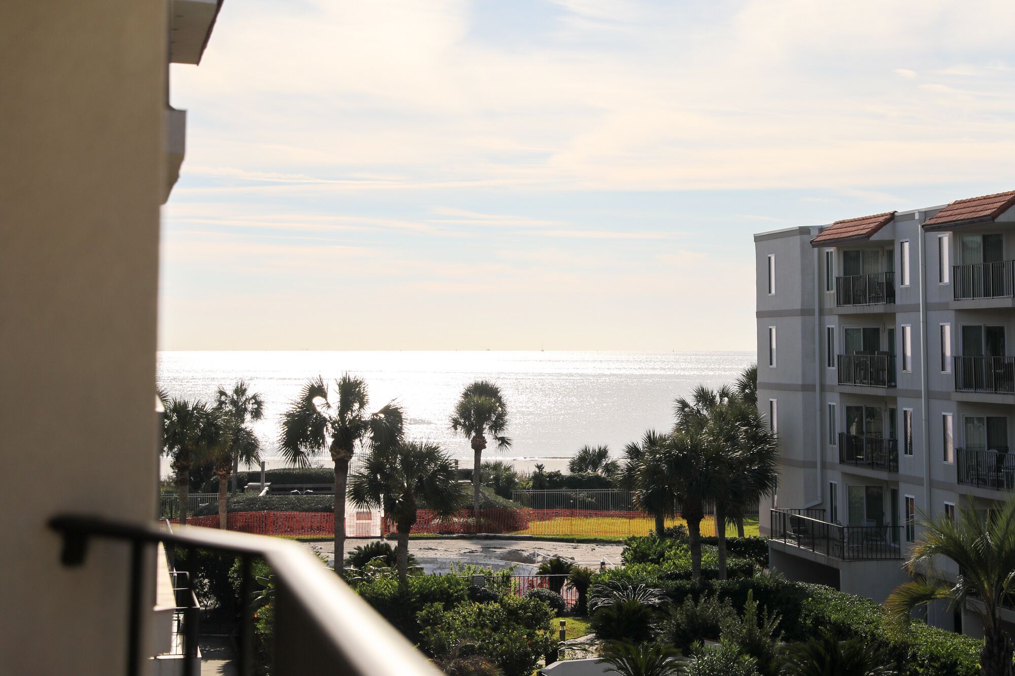 A balcony overlooking a beach with palm trees and a building with balconies.