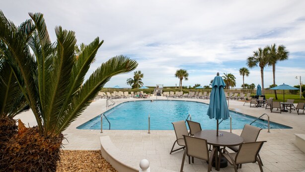 A swimming pool with lounge chairs and umbrellas, surrounded by palm trees and a clear sky.