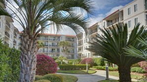 A multi-story residential building with balconies, surrounded by well-maintained gardens and palm trees.