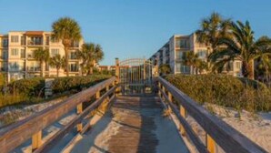 A wooden boardwalk leading to a gated entrance with buildings on either side.