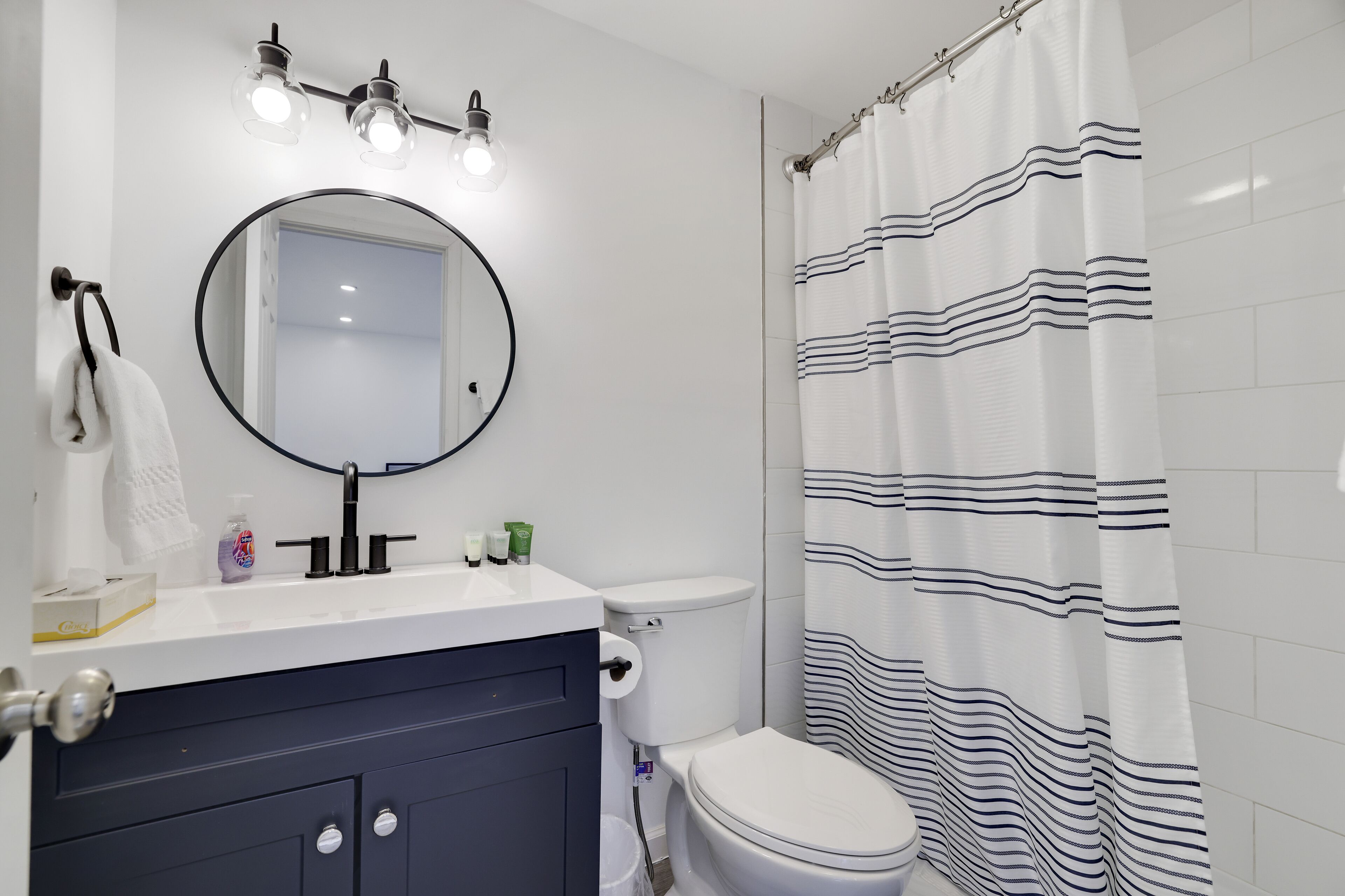 Une salle de bain avec un lavabo blanc, un miroir rond, des toilettes et un rideau de douche à rayures.