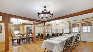 Un amplio comedor con vigas de madera, un candelabro y varias mesas dispuestas para comer.