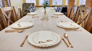 Una mesa de comedor dispuesta con platos blancos, cubiertos dorados y vasos transparentes, con un jarrón de flores en el centro.