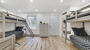 Una habitación con literas, un aparador de madera, una lavadora y una ventana con vistas a árboles.