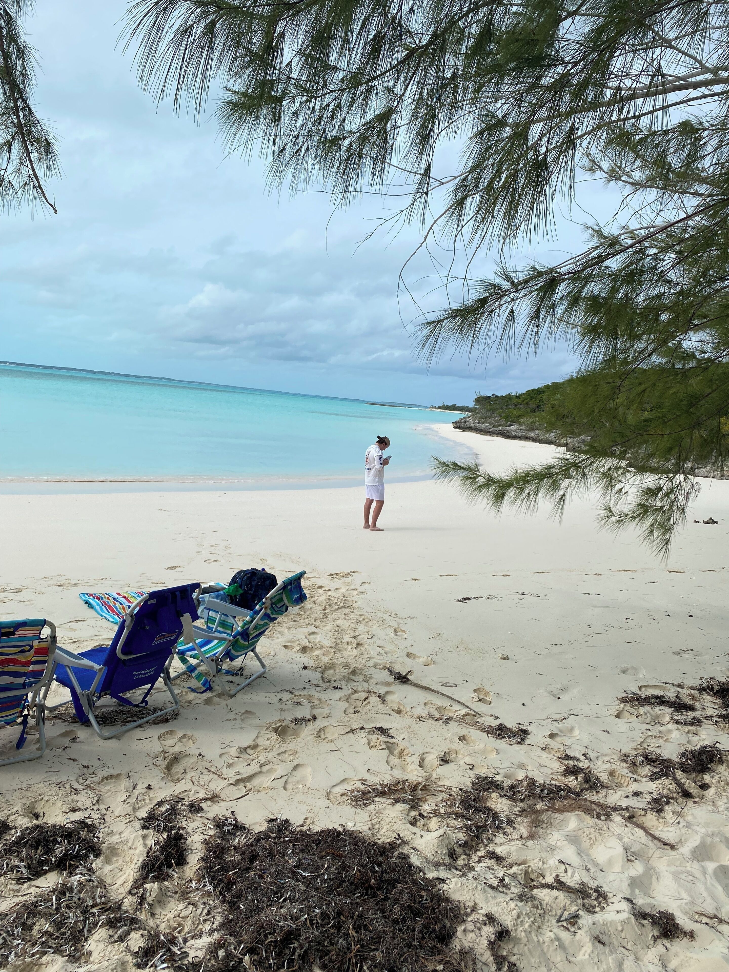 A beach with two blue beach chairs, one with a colorful towel, and a person walking towards the water.