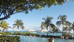A poolside table with drinks and a glass of water, overlooking a pool with umbrellas and palm trees. - Modern vacation home with private yard, steps to the beach and centrally located (Mt Thompson)