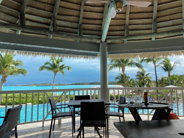 A covered outdoor area with a pool, dining table, chairs, and a view of the ocean.