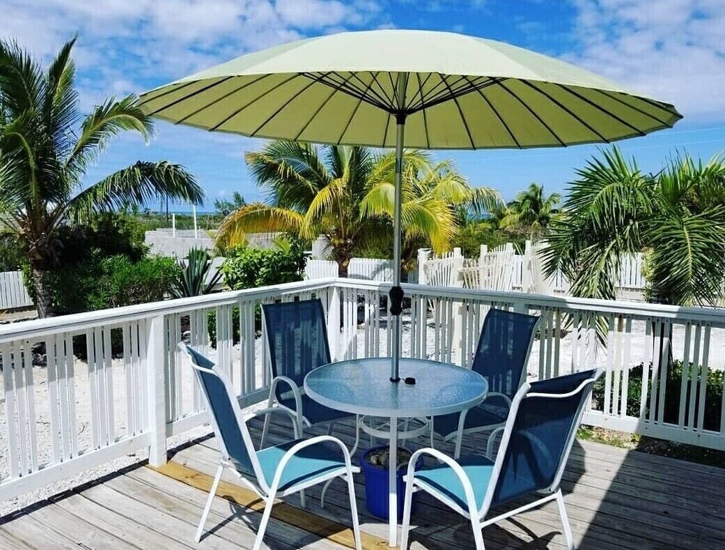 A deck with a round table and chairs, an umbrella, and a white picket fence.