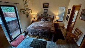 Ein Schlafzimmer mit einem Bett, Nachttischlampen, einem Holzstuhl, einem Fenster mit Jalousien und gerahmten Bildern an der Wand.