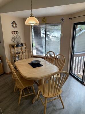 A dining area with a wooden table and chairs, a hanging light fixture, and a window with blinds.
