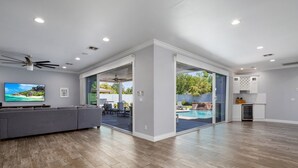 A spacious living room with a gray sectional sofa, a flat-screen TV, and a ceiling fan. - PARADISE IN ARCADIA NEAR SCOTTSDALE 5BED/4BATH + HEATED POOL (Phoenix)