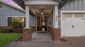 A two-story house with a covered porch, brick foundation, and a garage. - PARADISE IN ARCADIA NEAR SCOTTSDALE 5BED/4BATH + HEATED POOL (Phoenix)