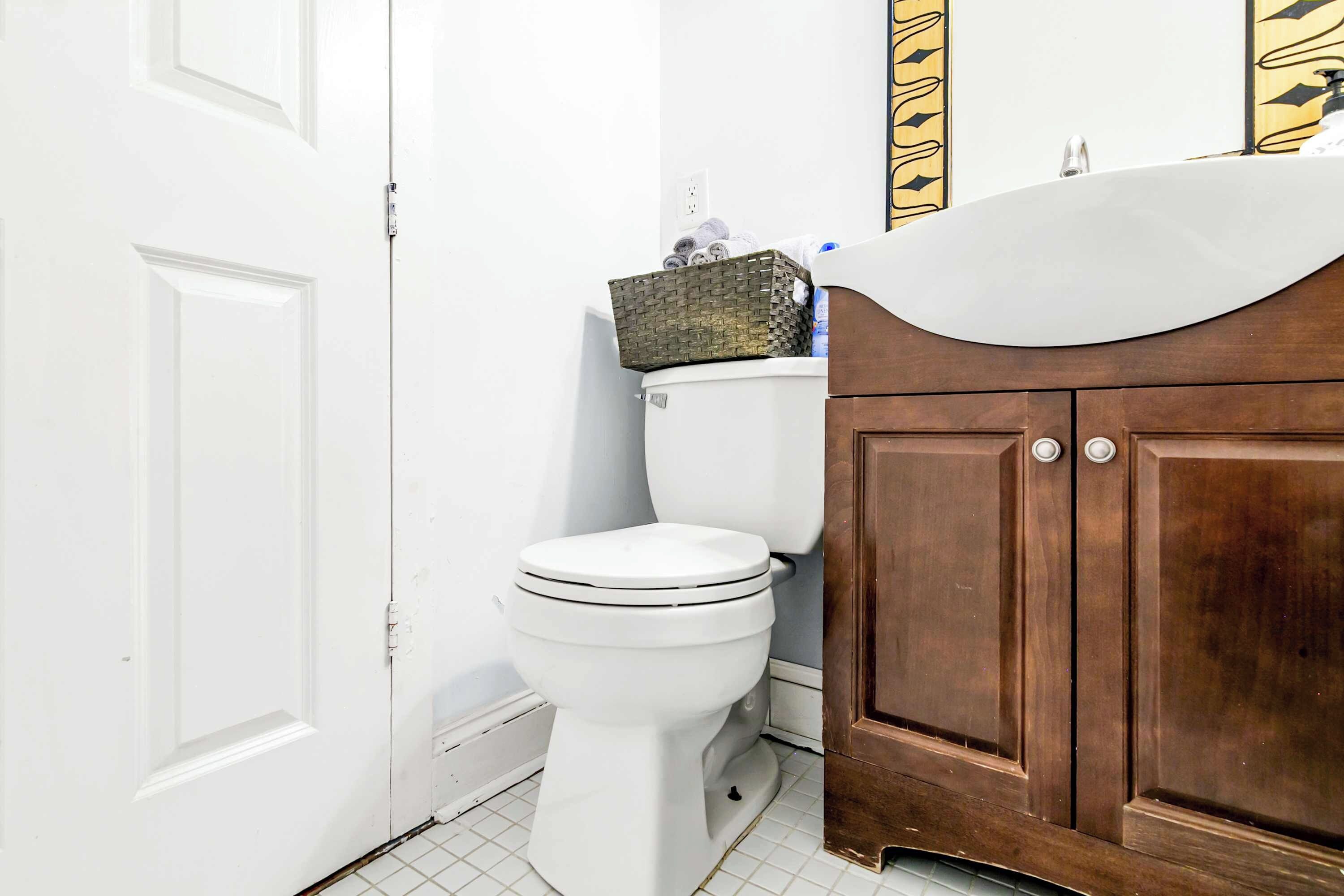 Een badkamer met een wit toilet, een houten wastafelmeubel met een wastafel en een betegelde vloer.