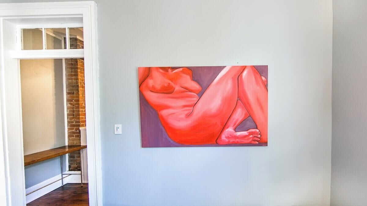 A room with a painting on the wall, a wooden bench, and a brick wall.